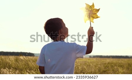 happy boy holding windmill his hand. portrait boy smile. childhood dream child. cheerful child holds spinner toy his hand sunset. play game sunset. little son child sunset park plays with spinner toy.