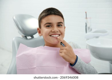 Happy boy holds finger near his mouth, looks at camera, smiles with beautiful toothy smile after receiving dental treatment in dentistry clinic. Oral hygiene, early prevention teeth diseases concept - Shutterstock ID 2069346008