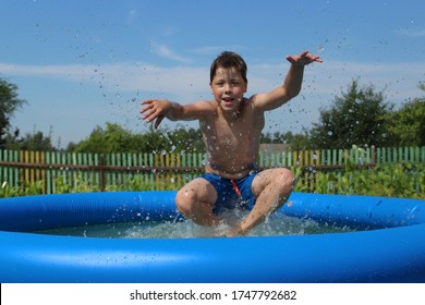 A Happy Boy Jumps With A Splash Into An Inflatable Swimming Pool. Splash In A Swimming Pool, Child Jumps Into The Water. Countryside, Backyard Swimming Pool.