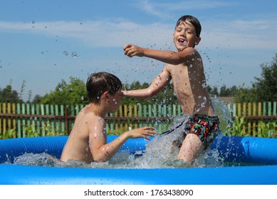 A Happy Boy Jumps With A Splash Into An Inflatable Swimming Pool. Splash In A Swimming Pool, Child Jumps Into The Water. Countryside, Backyard Swimming Pool. Children In Swimming Pool 