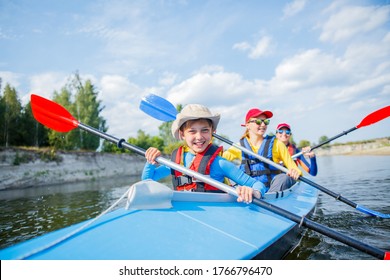 Happy Boy Kayaking On The River. Active Boy With His Sisters Having Fun And Enjoying Adventurous Experience With Kayak On A Sunny Day During Summer Vacation