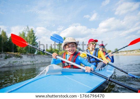 Happy boy kayaking on the river. Active boy with his sisters having fun and enjoying adventurous experience with kayak on a sunny day during summer vacation