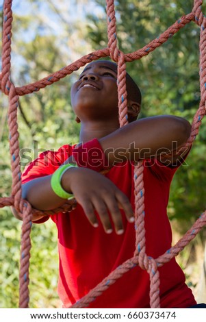Happy boy leaning on net during obstacle course in the boot camp
