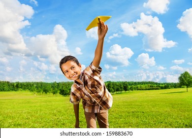 Happy Boy Leaning And Throwing Yellow Paper Airplane On Bright Sunny Day In The Field