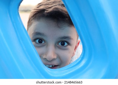 Happy Boy Looking Through Hole Of Climbing Toy In Park