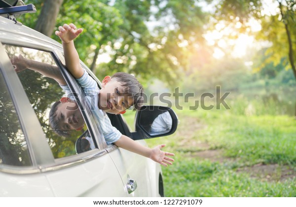 Happy boy looks out from auto window\
and greets somebody, Happy kids travel by the\
car