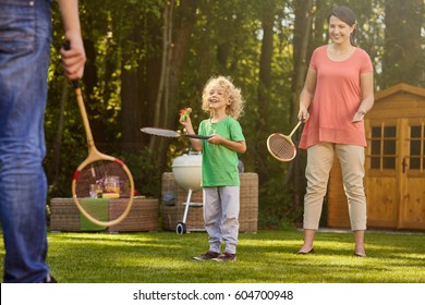 Happy Boy Playing Badminton With Parents In Garden