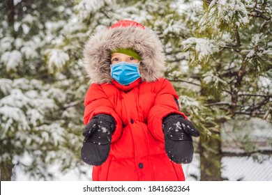 Happy Boy Plays With Snow Wearing A Medical Mask During COVID-19 Coronavirus. Cute Kid Throwing Snow In A Winter Park. Happy Winter Holidays. Winter Fashion