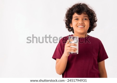 A HAPPY BOY POSING IN FRONT OF CAMERA WHILE HOLDING A GLASS OF MILK