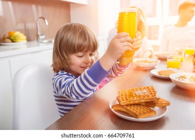 Happy Boy Pouring Honey On Waffles While Having Breakfast With Family