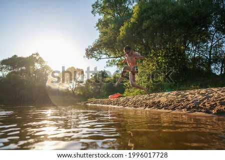 Happy boy run from the shore into the water. Summer children's vacation on shore of a lake or river. kid jump into water, swim and splash around at sunset. Active holidays. Dynamic image