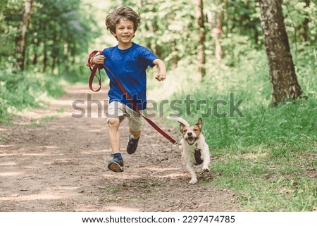 Happy boy running with dog on leash by park alley on summer day
