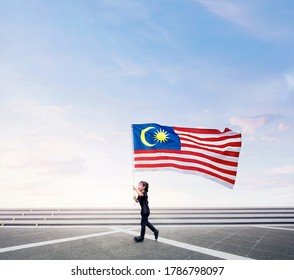 Happy Boy Running While Holding Malaysia Flag On Open Space. Happy National Day.