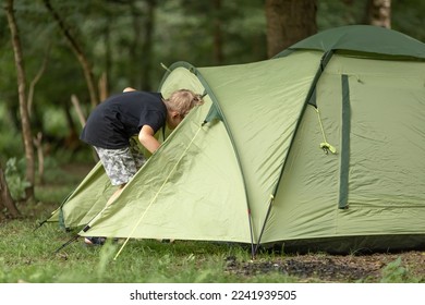 Happy boy scout looking entering his tent tot have some rest in the afternoon. Summer camping in the mountains, green forest on background. Little boy having a rest in the nature, enjoying fresh air - Powered by Shutterstock