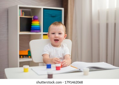 Happy boy sitting at a table with paints and brushes - Shutterstock ID 1791462068