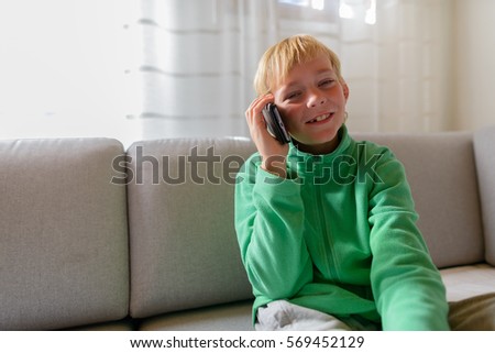 Happy boy smiling while talking on mobile phone and sitting on sofa at home
