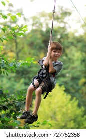 Happy Boy Successfully Passed The Obstacle Course In The Rope Park And Is Flying In The Air On The Zip Line Among Greenery And Lush Foliage