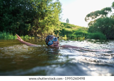 Happy boy in swimming glasses swims in the river in the summer at sunset. A child enjoys a summer children's holiday on the shore of the lake. Active holidays. Dynamic Image