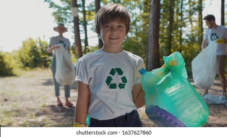 Happy boy voluteers activists child in gloves tidying up rubbish in park or forest look at camera smile save environmentplastic pollution bag bottle recycle ecology garbage nature care slow motion - Powered by Shutterstock