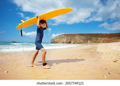 Happy boy in wetsuit walk with surfboard over head in hands return from sea to the beach