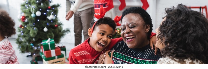 Happy Boy And Woman Hugging Laughing African American Granny Near Blurred Family And Christmas Tree, Banner