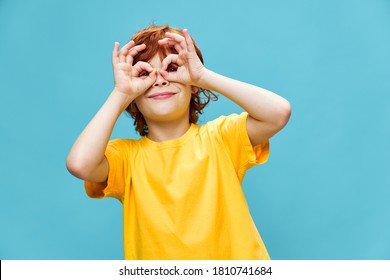 Happy boy in a yellow t-shirt holds joined fingers in front of his eyes  - Powered by Shutterstock