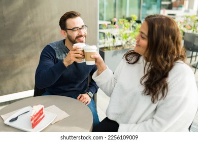 Happy boyfriend and big girlfriend making a toast with coffee while on a date at a cafe and eating a dessert