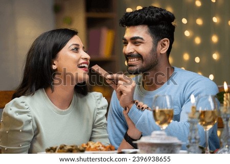 Happy boyfriend giving chocolate byte to girl friend during candle light dinner at restaurant - concept of valentine's day celebration, romantic couples and intimacy.