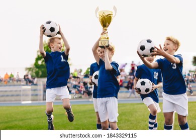 Happy Boys In Elementary School Sports Team Celebrating Soccer Succes In Tournament Final Game. Kids Winning Football Game. Happy Children Sports Team Rising Golden Trophy