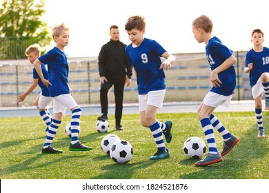 Happy Boys On A Sports Training Class With Young Coach. School Age Children Making Sport. Kids Kicking Soccer Ball On Summer Football Camp