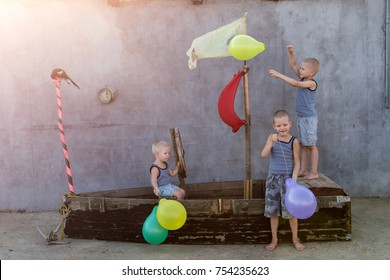 Happy boys play pirates and seafarers. Three brothers have fun together. The old boat is decorated with balloons.