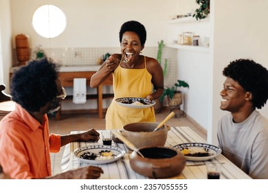 Happy Brazilian family gathers at the table for a traditional meal. Dad and son enjoy the delicious cuisine while mom tastes food from her plate. Clay pots filled with Brazilian dishes fill the table. - Powered by Shutterstock