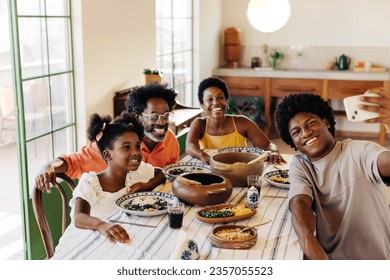 Happy Brazilian family sitting at the table for a traditional meal, with clay pots filled with delicious dishes. They smile and pose for a selfie, creating memories in their kitchen. - Powered by Shutterstock