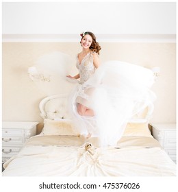 Happy bride with dark blonde hair jumps on the bed