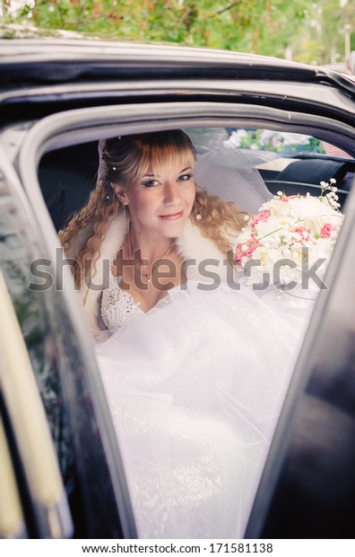 happy bride with flower bouquet siting in\
the car. Portrait of a pretty bride in a\
car