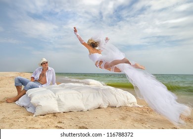 Happy Bride flying on bed to her husband on the beach