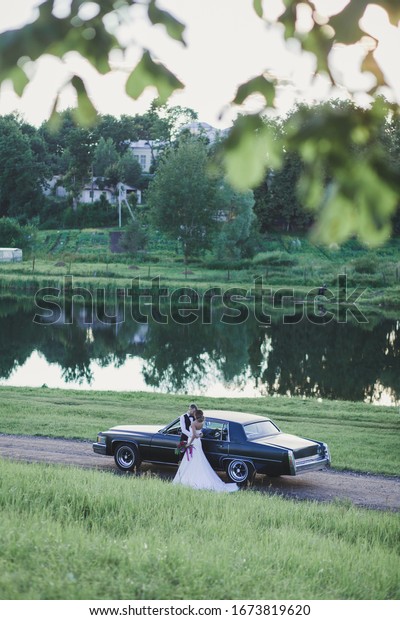 Happy\
bride and groom hugging near old retro car\
outdoors