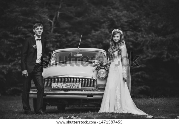 Happy\
bride and groom, newlywed wedding couple near a retro car on a\
country for honeymoon after the ceremony. The best day and\
marriage. Just married. Black and white\
photo.