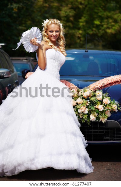 Happy bride near\
wedding car with flowers
