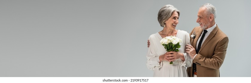 Happy Bride In Wedding Dress Holding Bouquet And Standing With Middle Aged Groom In Suit Isolated On Grey, Banner