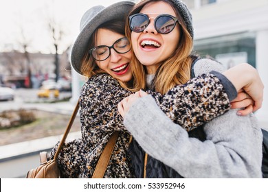 Happy brightful positive moments of two stylish girls hugging on street in city. Closeup portrait funny joyful attarctive young women having fun, smiling, lovely moments, best friends