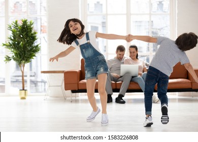 Happy brother and sister holding hands and spin. Smiling siblings children have fun and enjoy with dance on background with parent using laptop.