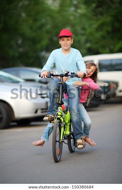 Happy brother and sister ride bicycle near car\
parking at summer day.