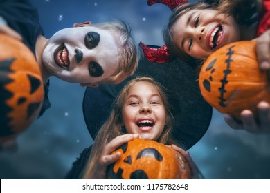 Happy Brother And Two Sisters At Halloween. Funny Kids In Carnival Costumes Outdoors. Cheerful Children And Pumpkins Buckets On Night Sky Background.