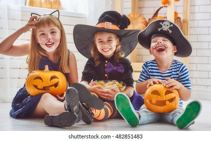 Happy brother and two sisters on Halloween. Funny kids in carnival costumes indoors. Cheerful children play with pumpkins and candy.
