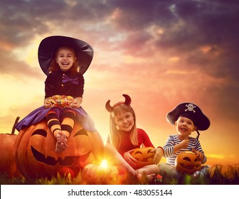 Happy brother   two sisters Halloween  Funny kids in carnival costumes outdoors  Cheerful children   pumpkins sunset background 