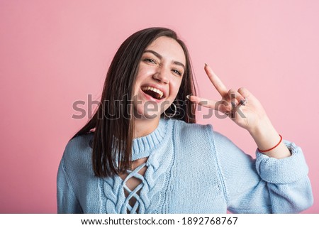 Happy brunette girl showing peace sign in studio on pink background