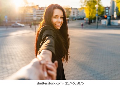 Happy brunette girl with a smile on her face holding boyfriend's hand on a street at sunset on a warm spring,summer evening.Follow-me concept.Selective focus.