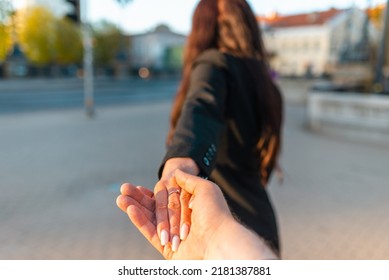Happy brunette girl turn away face holding boyfriend's hand on a street at sunset on a warm spring,summer evening.Follow-me concept.Selective focus.