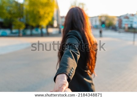 Happy brunette girl turn away face holding boyfriend's hand on a street at sunset on a warm spring,summer evening.Follow-me concept.Selective focus.